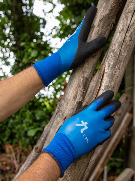 Person wearing blue gardening gloves with black accents on a wooden branch outdoors.