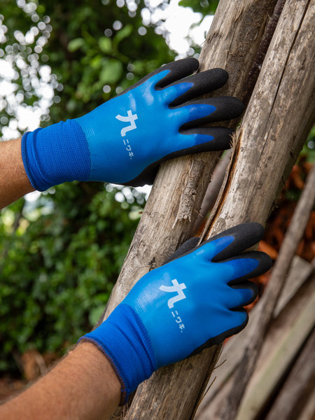 A person wearing blue gardening gloves with black fingertips holds a wooden log outdoors.