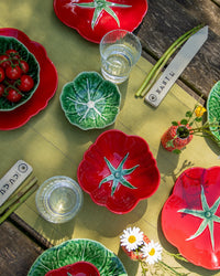 Colorful ceramic plates with tomato design on a wooden table with glasses and flowers.