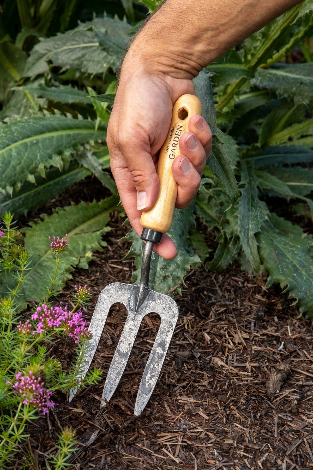 Hand holding a garden fork with a wooden handle among plants