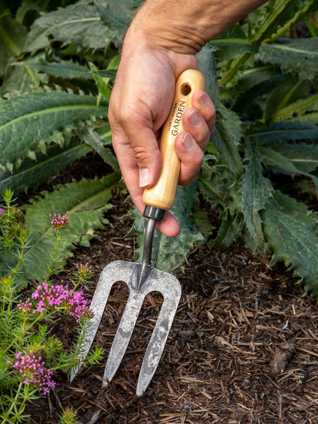 Hand holding a garden fork with a wooden handle among plants