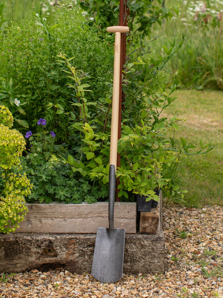 Garden spade leaning against a wooden crate with greenery in the background