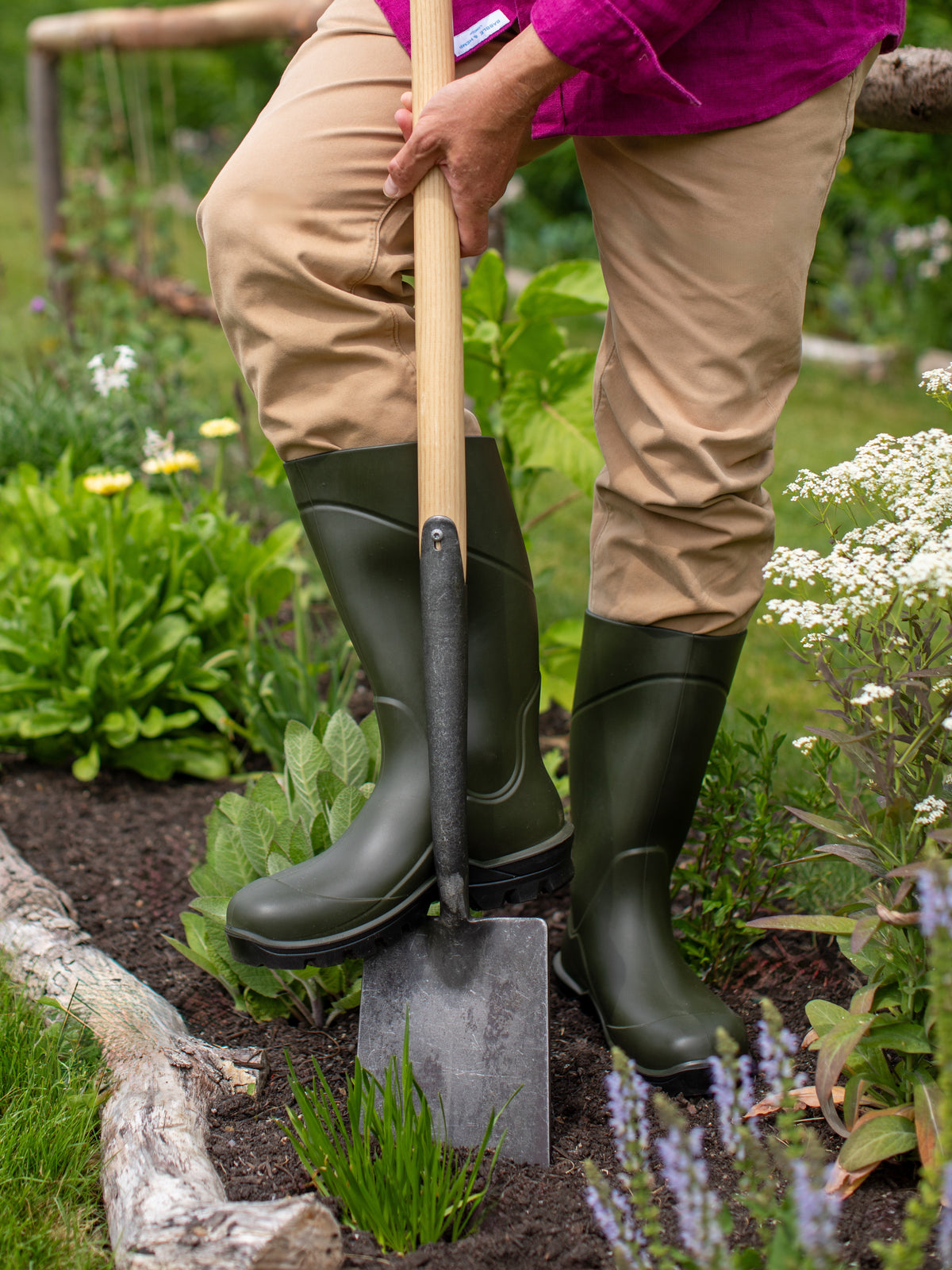 Person wearing green Wellington boots holding a spade in a garden setting