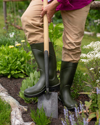 Person wearing green Wellington boots holding a spade in a garden setting