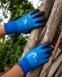 A person wearing blue gardening gloves with black fingertips holds a wooden log outdoors.