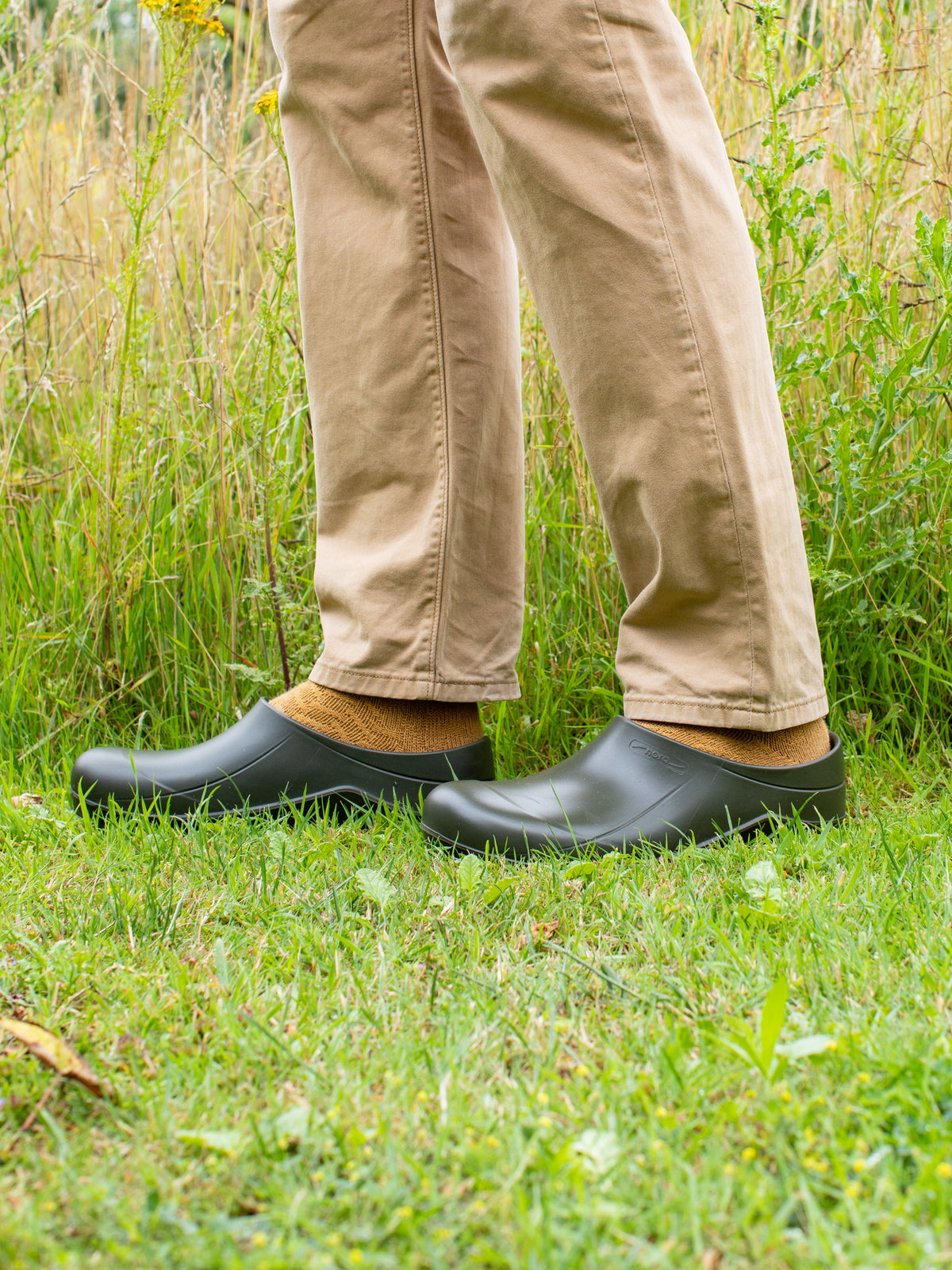 Person wearing green clogs and beige trousers standing on grass