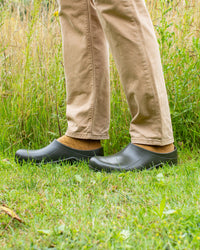 Person wearing green clogs and beige trousers standing on grass