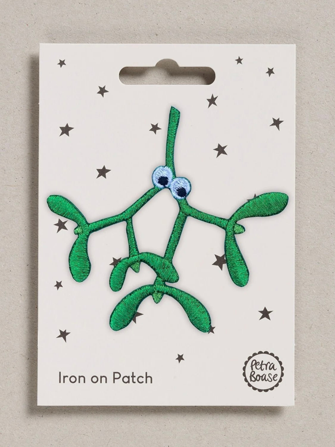 A green embroidered mistletoe iron-on patch with googly eyes, displayed on its white backing card featuring black stars and the text 'Iron on Patch' and 'Petra Boase'.
