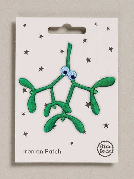 A green embroidered mistletoe iron-on patch with googly eyes, displayed on its white backing card featuring black stars and the text 'Iron on Patch' and 'Petra Boase'.