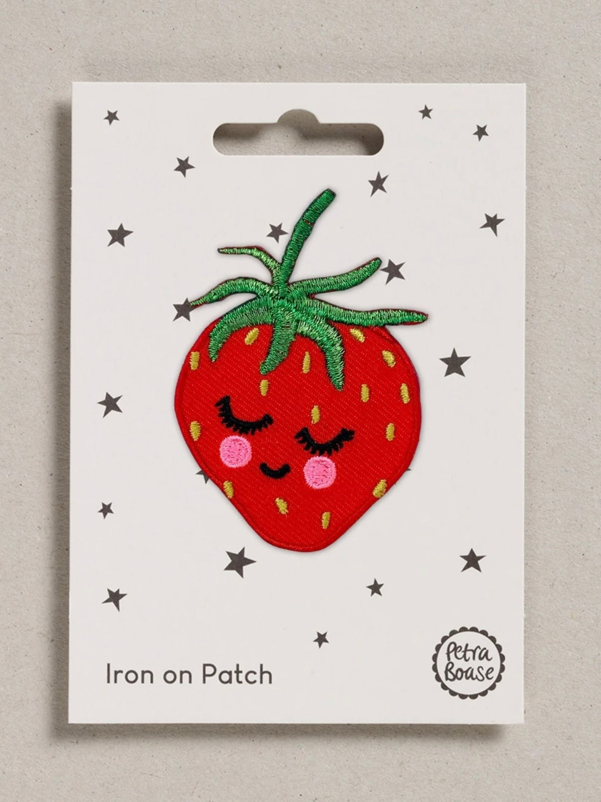 Iron-on patch of a red strawberry with a smiling, blushing face design on a white card with star patterns.