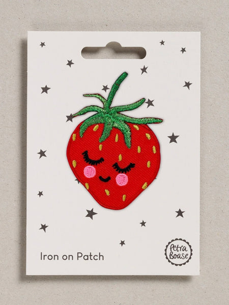 Iron-on patch of a red strawberry with a smiling, blushing face design on a white card with star patterns.