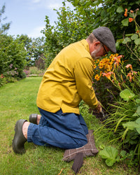 Man in yellow jacket and blue trousers gardening in a lush green garden.
